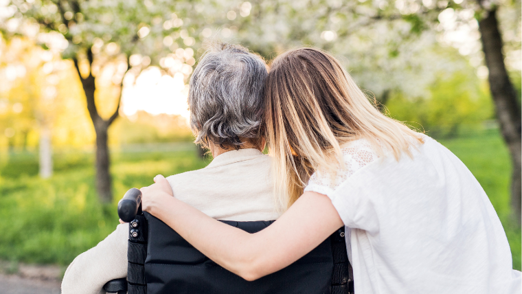 Daughter embracing her elderly parent in a wheelchair outdoors, representing family caregivers arranging medical transportation
